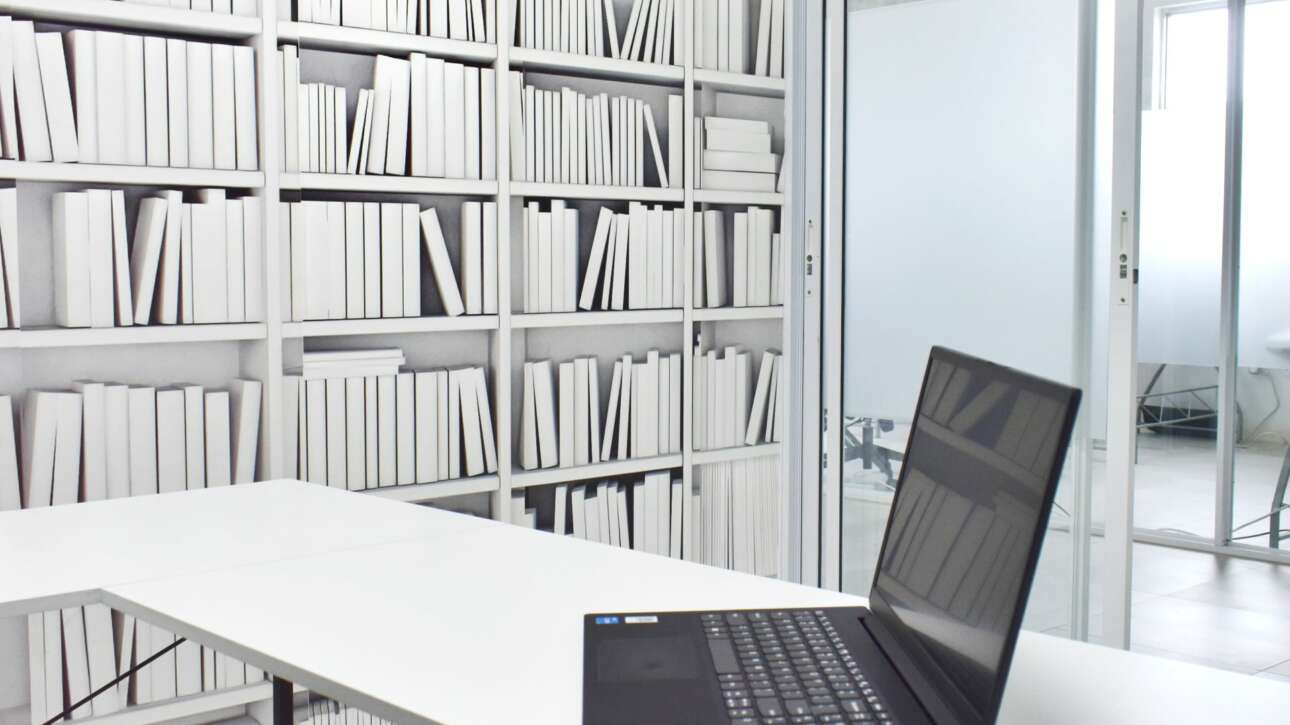 The transom above each office partition facilitates the flow of light throughout the space and a sepia toned bookcase mural creates a neutral backdrop for video calls